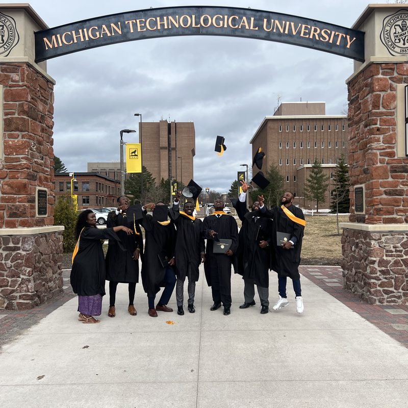 Graduates in caps and gowns walking through a university entrance arch